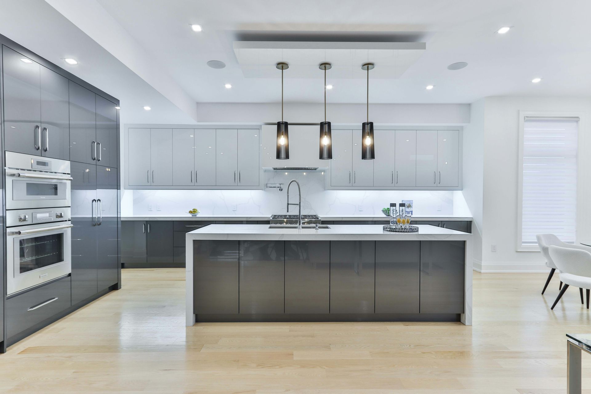 A modern kitchen with grey cabinets, a white island, and three pendant lights